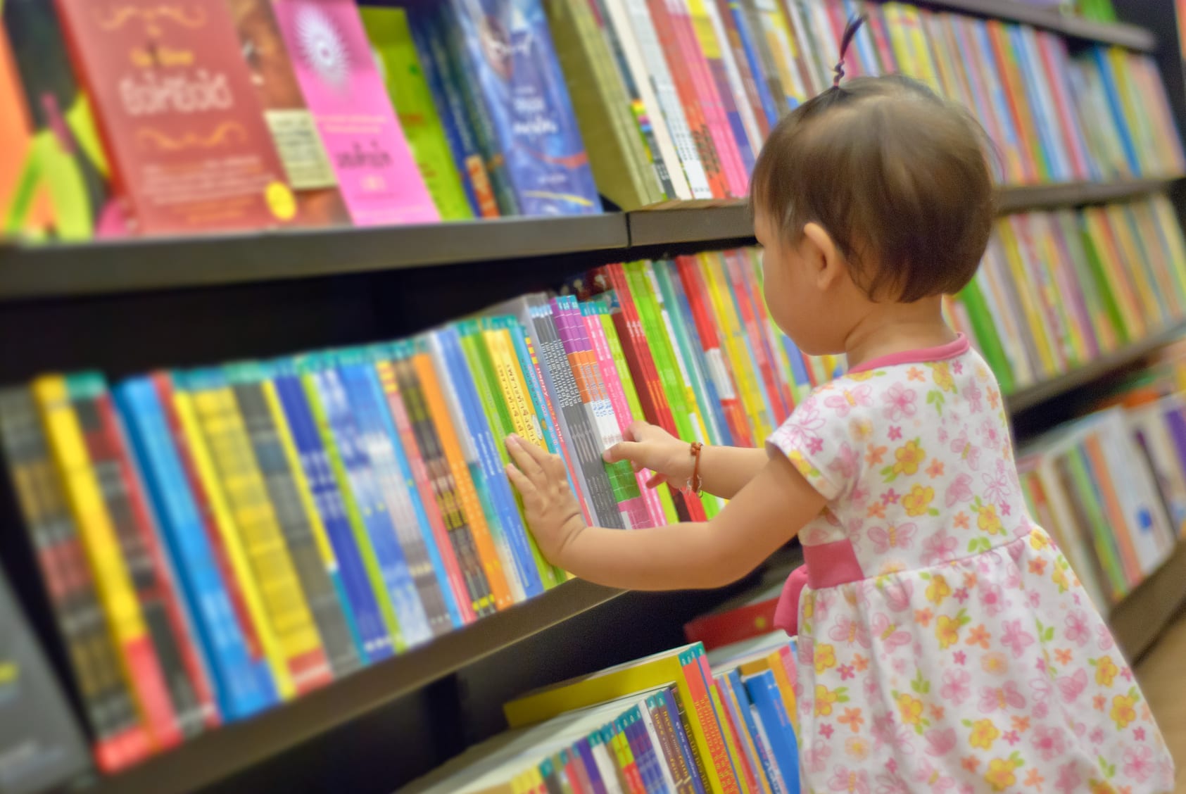 Asian Little girl is choosing a book in the library. A child is looking at the books in the library deciding which one to take home. Children creativity and imagination.